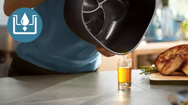 Fat being poured out of the Philips Airfryer pan into a glass, with the cooked chicken beside it