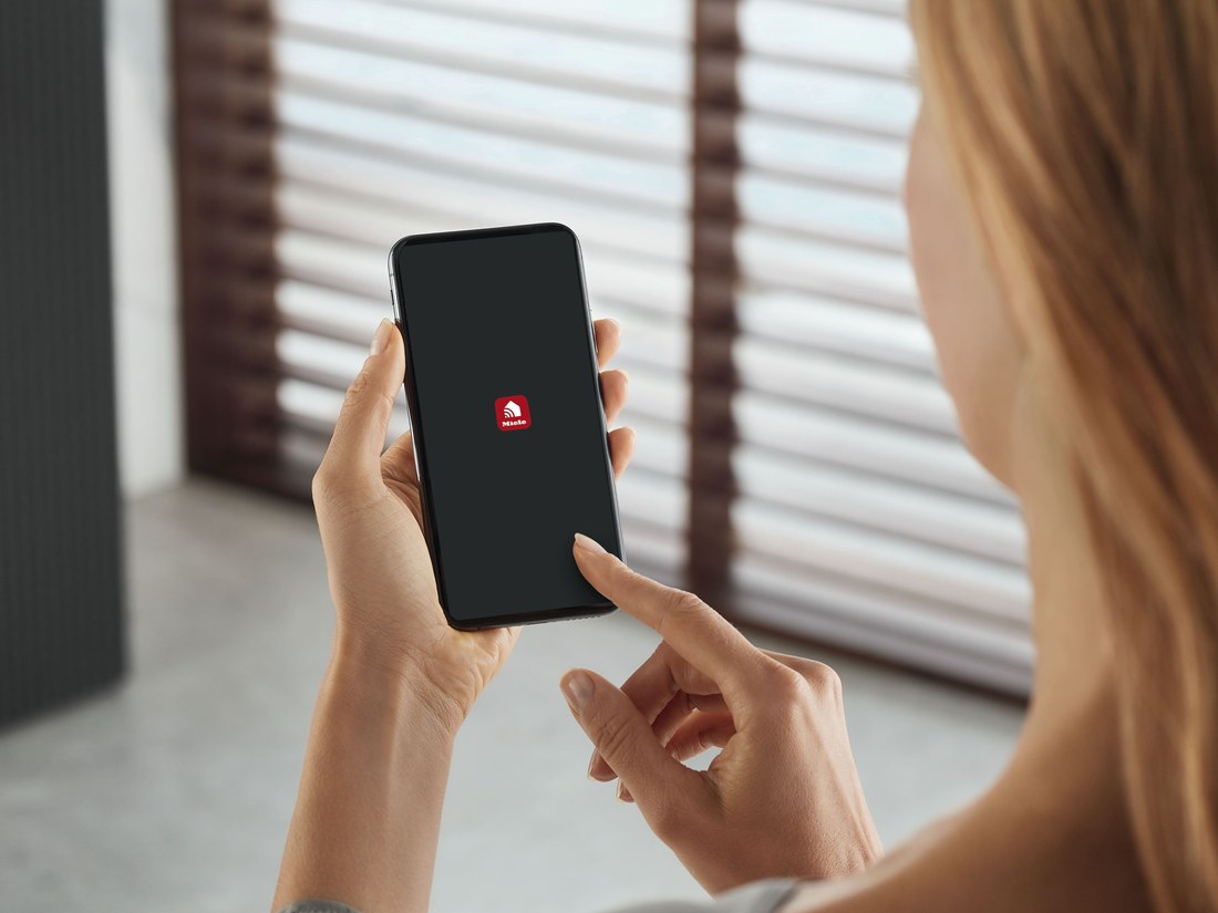 Hand holding smartphone opening the Miele app